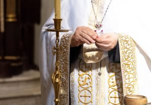 A priest wearing ornate vestments performs a sacred ritual in a church.