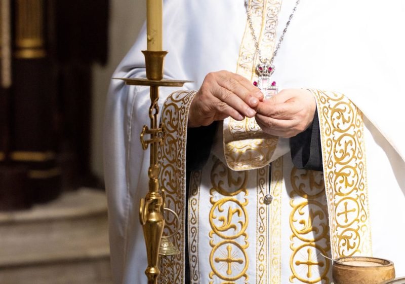A priest wearing ornate vestments performs a sacred ritual in a church.