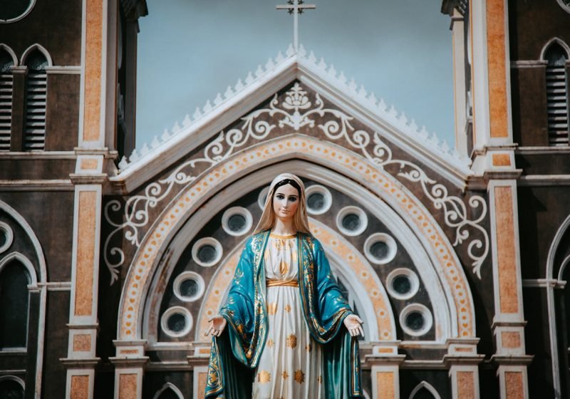 Vibrant statue of the Virgin Mary in front of an ornate church facade.